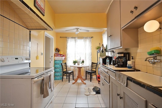 kitchen featuring light tile patterned floors, decorative backsplash, white electric range oven, a ceiling fan, and a sink