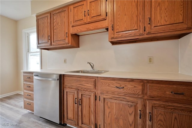 kitchen featuring a sink, light countertops, light wood-style floors, stainless steel dishwasher, and brown cabinets