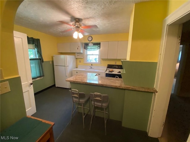 5208 Orchard Park Dr, Parma, OH 44134 - kitchen with electric range oven, a peninsula, freestanding refrigerator, white cabinets, and a ceiling fan