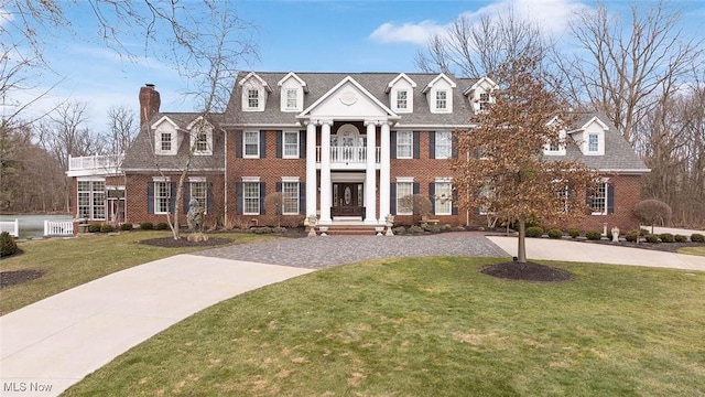 neoclassical / greek revival house with brick siding, curved driveway, a chimney, and a front yard