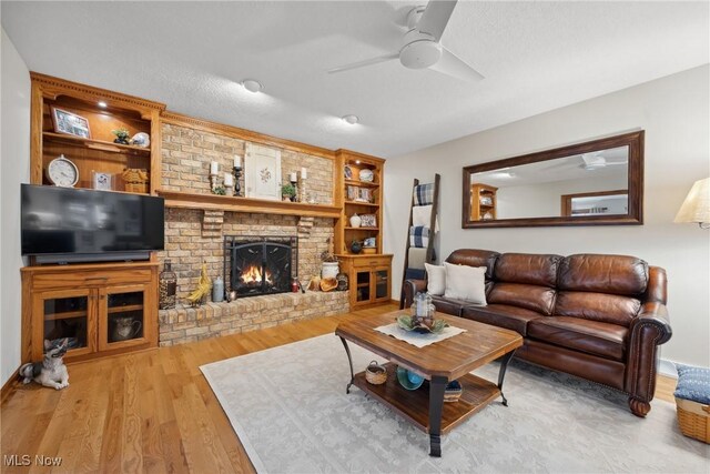 living area with built in features, wood finished floors, a ceiling fan, a fireplace, and a textured ceiling