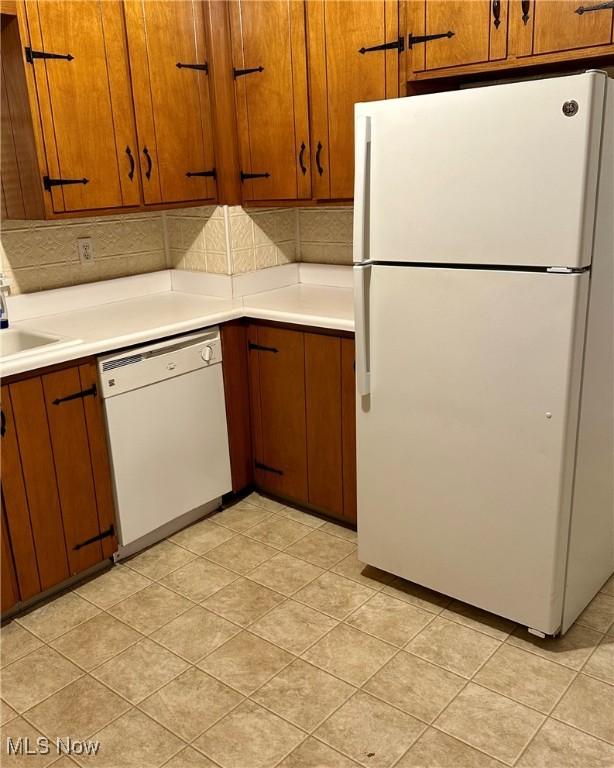 kitchen featuring tasteful backsplash, white appliances, light countertops, and brown cabinetry