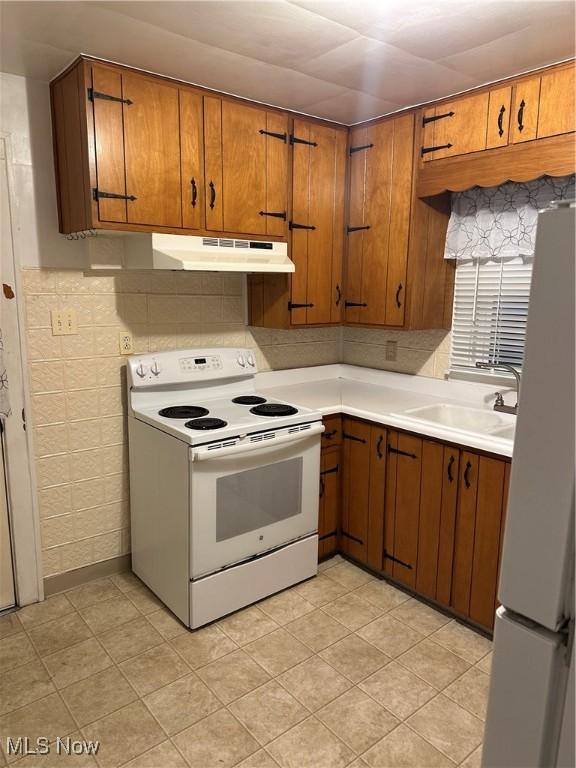 kitchen with under cabinet range hood, a sink, white appliances, brown cabinetry, and light countertops