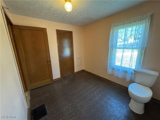 unfurnished bedroom with visible vents, a textured ceiling, baseboards, and multiple closets