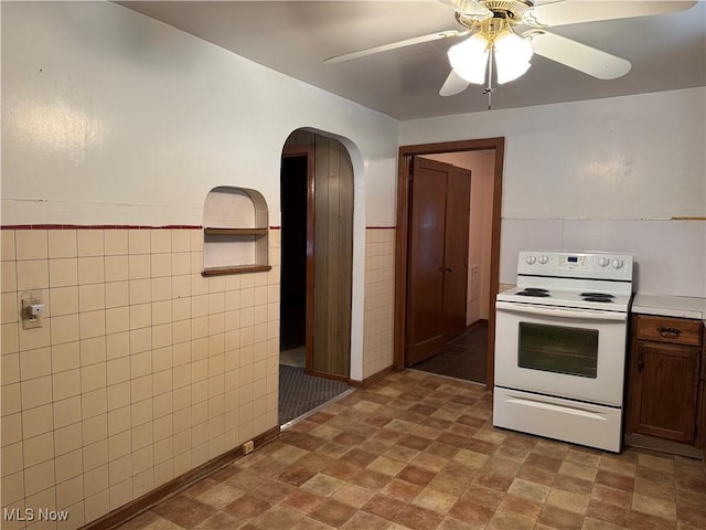 kitchen featuring wainscoting, arched walkways, electric range, tile walls, and a ceiling fan