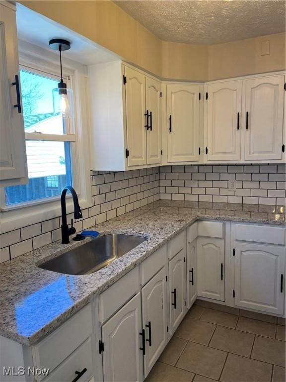 kitchen featuring white cabinetry, backsplash, light stone countertops, and a sink