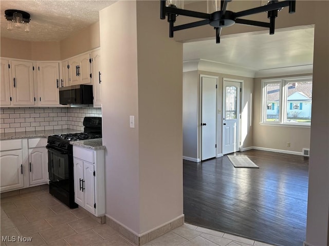 kitchen with black range with gas stovetop, backsplash, white cabinetry, light stone countertops, and stainless steel microwave