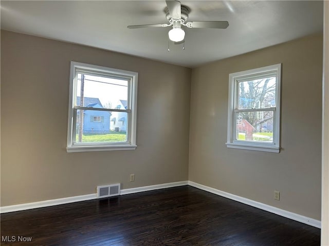 spare room featuring baseboards, visible vents, ceiling fan, and dark wood-type flooring