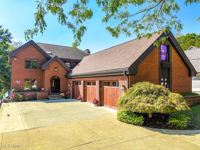 view of front facade featuring brick siding, driveway, an attached garage, and a shingled roof