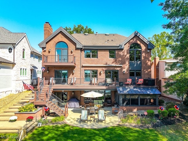 rear view of house with a patio, roof with shingles, a chimney, stairs, and brick siding