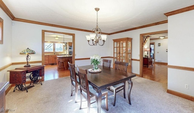 dining space with light wood finished floors, ornamental molding, a chandelier, and light carpet