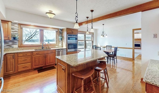 kitchen featuring brown cabinetry, stainless steel appliances, light wood-type flooring, and a sink