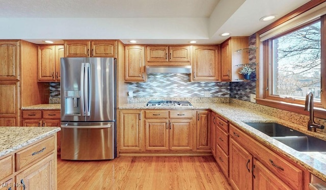 kitchen with light stone countertops, a sink, light wood-style floors, appliances with stainless steel finishes, and wall chimney range hood