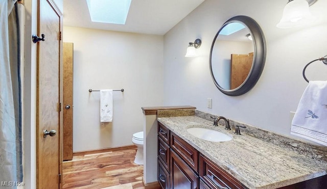 full bathroom featuring toilet, a skylight, vanity, and wood finished floors