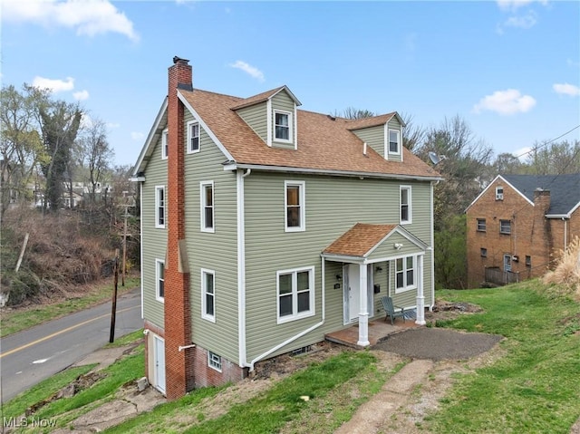 view of front of home featuring a chimney, a front yard, covered porch, and roof with shingles