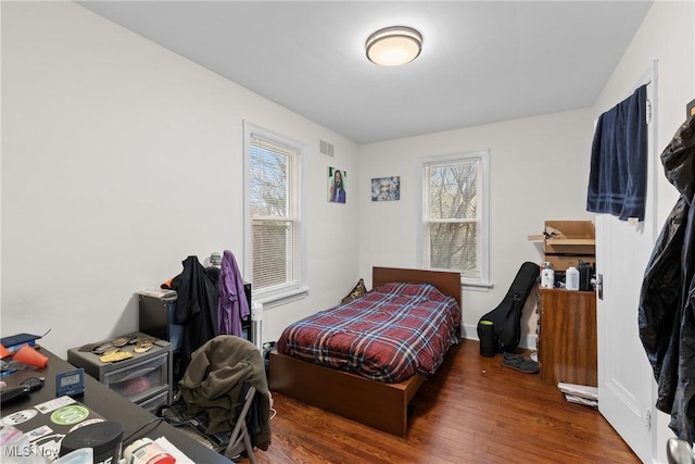 bedroom with baseboards, visible vents, and wood finished floors