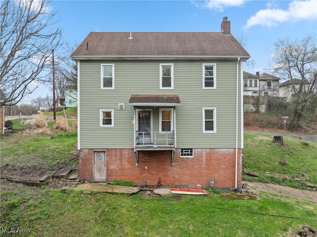 rear view of property with roof with shingles, brick siding, a yard, and a chimney