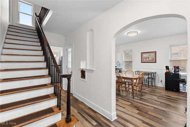staircase featuring baseboards, wood finished floors, and arched walkways