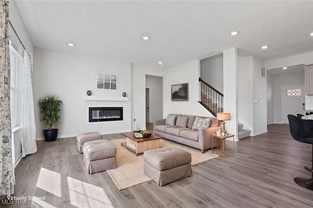 living area with recessed lighting, wood finished floors, a wealth of natural light, and stairway