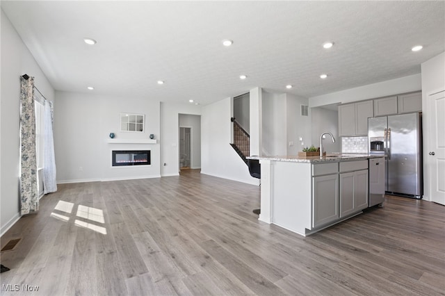 kitchen featuring a sink, gray cabinets, visible vents, stainless steel fridge with ice dispenser, and an island with sink