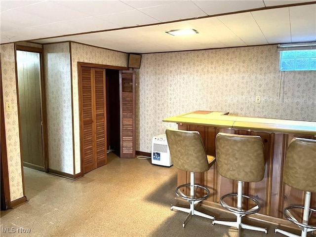 bar featuring wallpapered walls, a bar, and baseboards