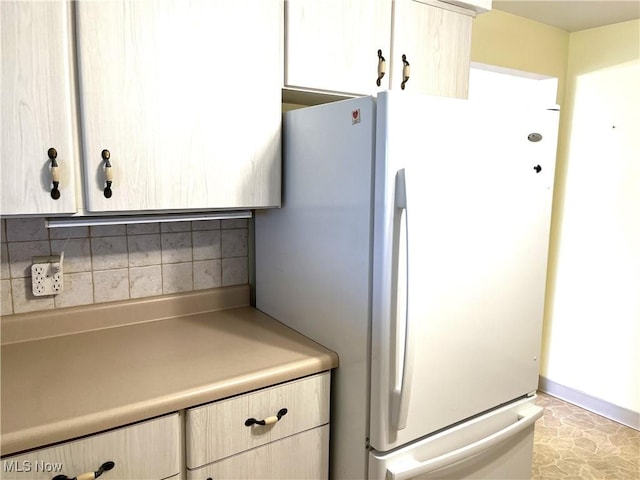 kitchen with light brown cabinetry, backsplash, light countertops, and freestanding refrigerator