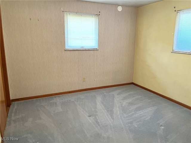 carpeted spare room featuring wallpapered walls and baseboards