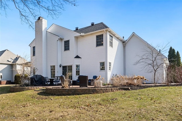 rear view of property with a chimney, a patio area, and a lawn
