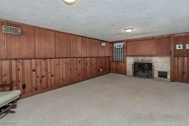 unfurnished living room with visible vents, wooden walls, carpet floors, a stone fireplace, and a textured ceiling