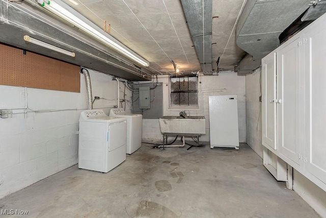 unfinished below grade area with a sink, concrete block wall, freestanding refrigerator, and separate washer and dryer