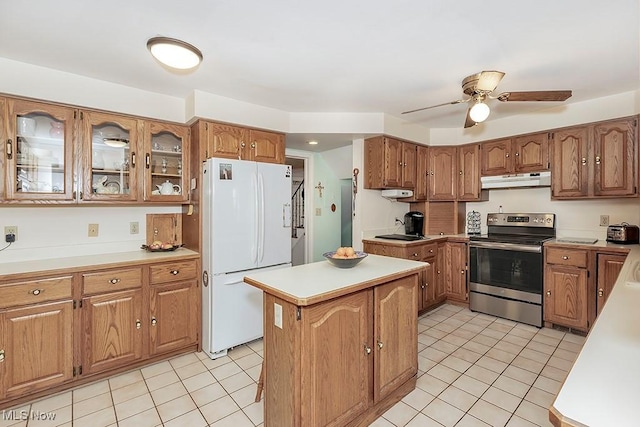 kitchen featuring under cabinet range hood, brown cabinets, stainless steel range with electric cooktop, and freestanding refrigerator