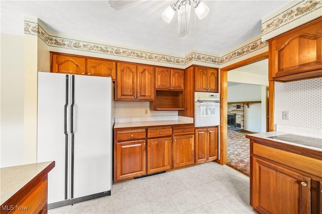 kitchen featuring white appliances, brown cabinetry, a ceiling fan, light countertops, and tasteful backsplash