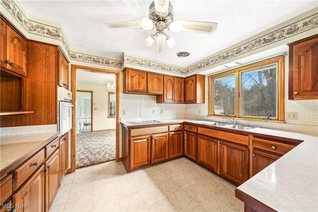 kitchen featuring oven, brown cabinets, a sink, light countertops, and black electric cooktop