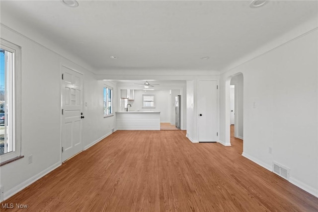 unfurnished living room featuring light wood-style flooring, visible vents, ceiling fan, arched walkways, and a sink