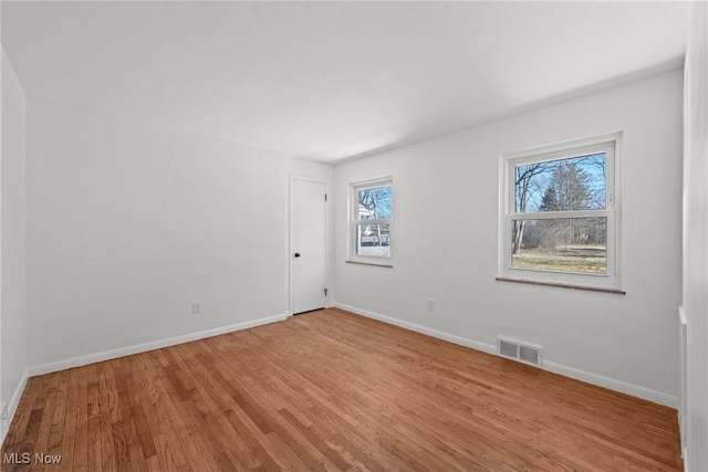 spare room featuring light wood finished floors, baseboards, and visible vents