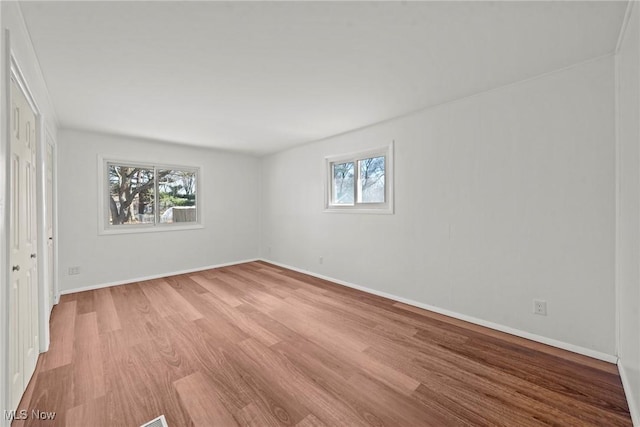 empty room with baseboards, plenty of natural light, and light wood-style floors