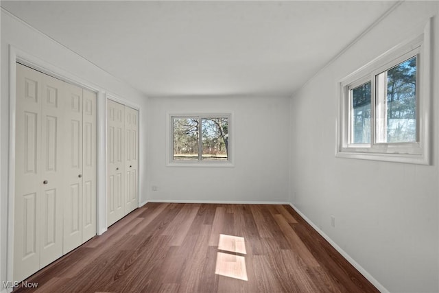 unfurnished bedroom with multiple closets, baseboards, and dark wood finished floors