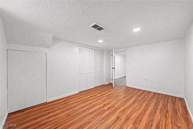 finished basement with a textured ceiling, visible vents, recessed lighting, wood finished floors, and baseboards