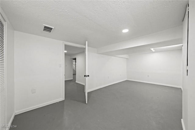 finished below grade area featuring visible vents, a textured ceiling, and baseboards