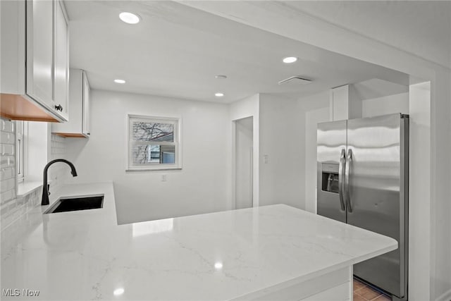 kitchen featuring light stone countertops, a peninsula, stainless steel refrigerator with ice dispenser, a sink, and decorative backsplash