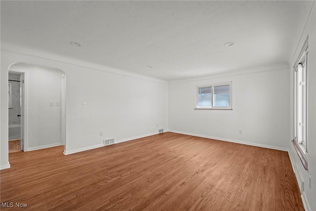spare room with arched walkways, wood finished floors, baseboards, and visible vents