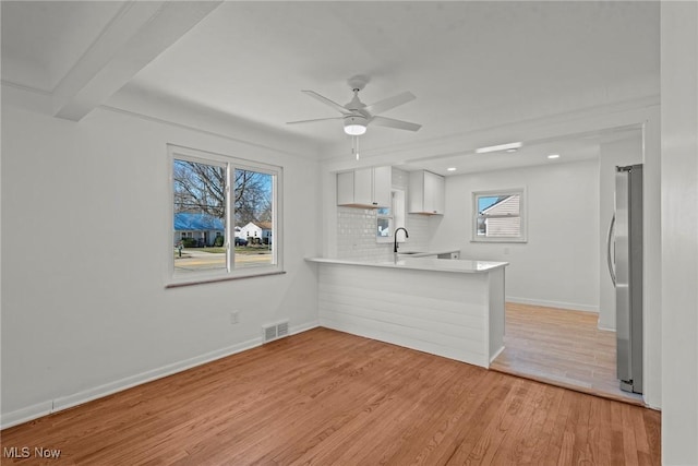 kitchen featuring freestanding refrigerator, light countertops, a sink, light wood finished floors, and backsplash
