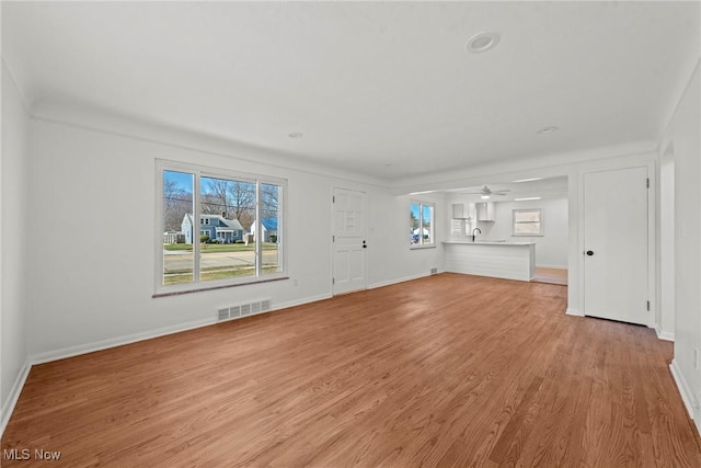 unfurnished living room with visible vents, light wood-style flooring, a ceiling fan, and baseboards