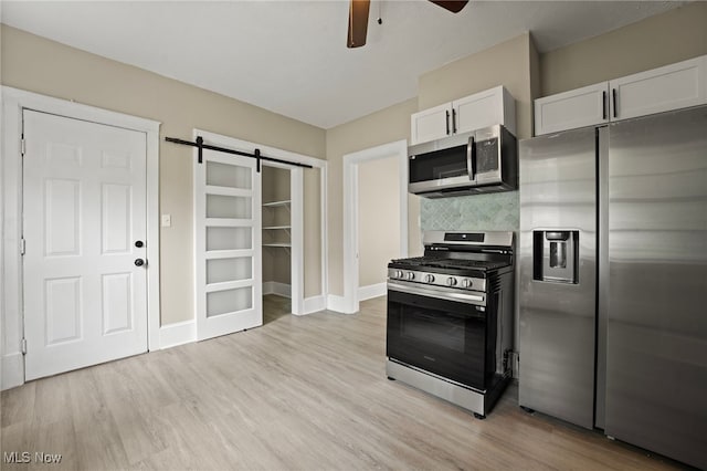 1344 E 112th St, Cleveland, OH 44106 - kitchen featuring light wood-style flooring, ceiling fan, appliances with stainless steel finishes, a barn door, and backsplash