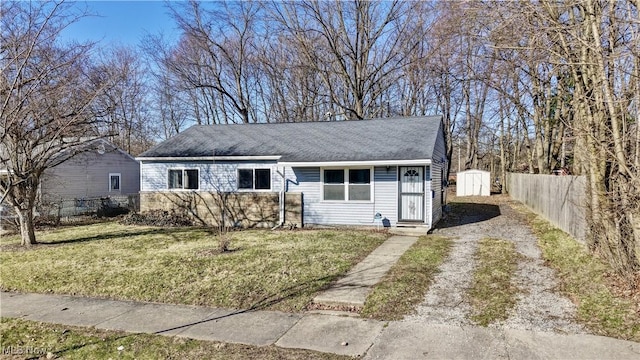 view of front facade with driveway, a storage shed, a front yard, and fence