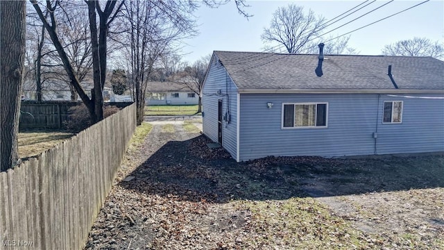 rear view of house with a shingled roof and fence