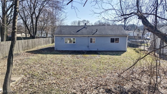 rear view of property featuring a yard, a shingled roof, and a fenced backyard