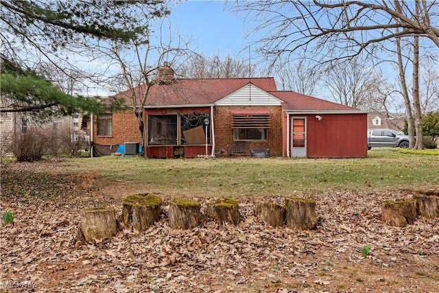 back of house featuring cooling unit, a sunroom, a chimney, a lawn, and brick siding