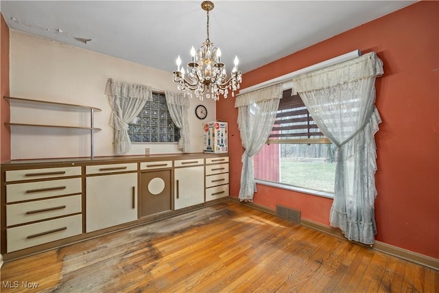 unfurnished dining area with visible vents, baseboards, a notable chandelier, and hardwood / wood-style flooring