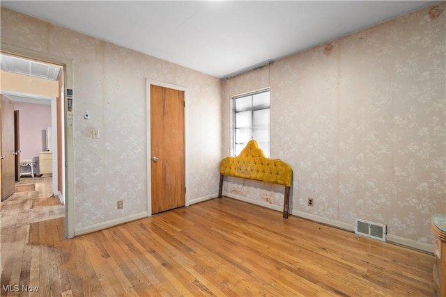 empty room featuring visible vents, hardwood / wood-style flooring, wallpapered walls, baseboards, and attic access